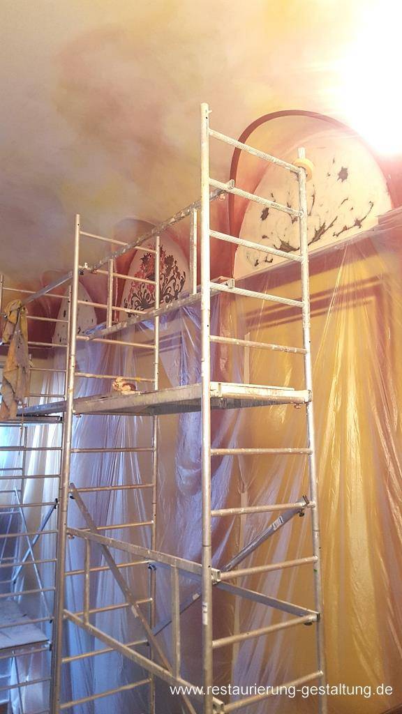 Gestalten der Wandbilder in Stil und Form der Neo - Renaissance. Da in den Wandauslässen nichts nachweisbar war, hat der Restaurator im Handwerk Norbert Schimpf Ornamente die sich im Treppenkopf befinden abgenommen und in die Wandauslässe mittels Schablone und Pausen hinein gemalt. Die Wandbilder wurden zum Abschluss der Oberwandgestaltung bemalt, da es für den Maler - Künstler einfacher ist die Farbigkeit an den Marmor anzupassen als, das man den Farbton des Marmors an die Gemälde anpasst. Während der Bemalung der Wandornamente wurde der Der Himmel in einer Lasurtechnik lasiert. Der Vorteilhierbei ist, das Restaurator Schimpf die die selben Farben verwenden kann. So entsteht eine Einheit zwischen den verschiedenen Bauteilen.